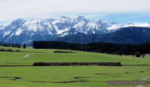 218.469 and RB57343 silhouetted against the green fields near Weizern-Hopferau with the 2000m peaks of the Tannheimer Berge, across the border in Austria, providing the background.